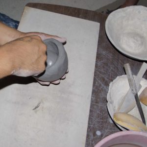 Using a piece of a gourd to work the clay on the inside