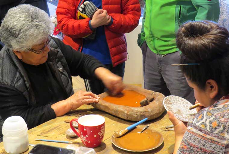 Rebecca Lucario preparing some orange paint while her daughter Amanda paints with a vegetal black