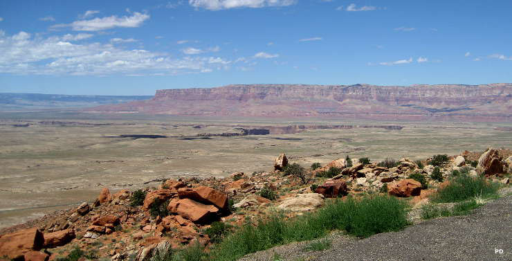 A view off the edge of Third Mesa near Old Oraibi with a flat green tableland below that is cut by a deeper canyon