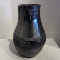 A tall black-on-black jar with a geometric design around the neck and an avanyu design around the shoulder