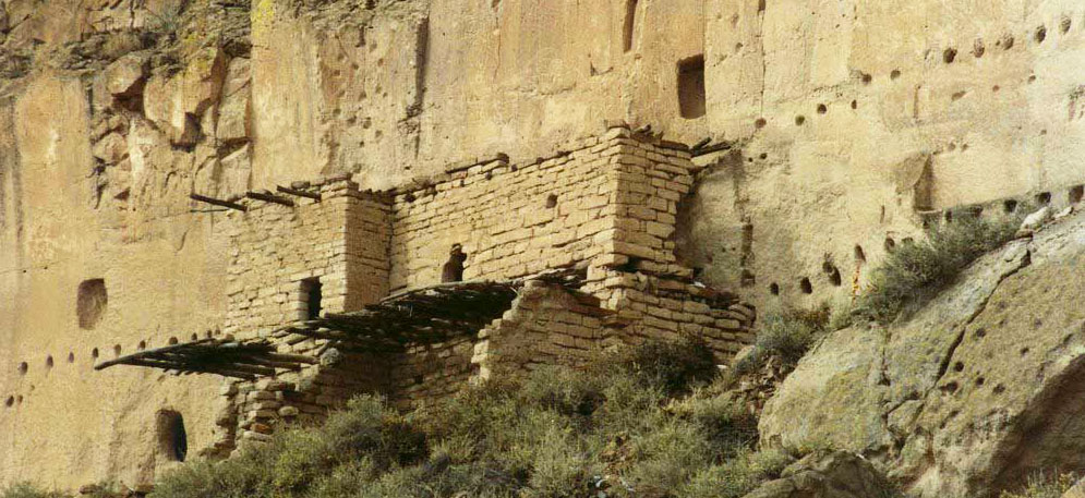 A stacked-stone building on the side of a cliff marked with the holes of former roof beams in ancient Puye, a ruin of the Santa Clara people