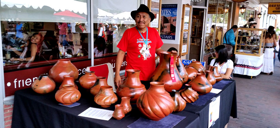 Dineh potter Samuel Manymules with his display of Dineh pottery at Santa Fe Indian Market